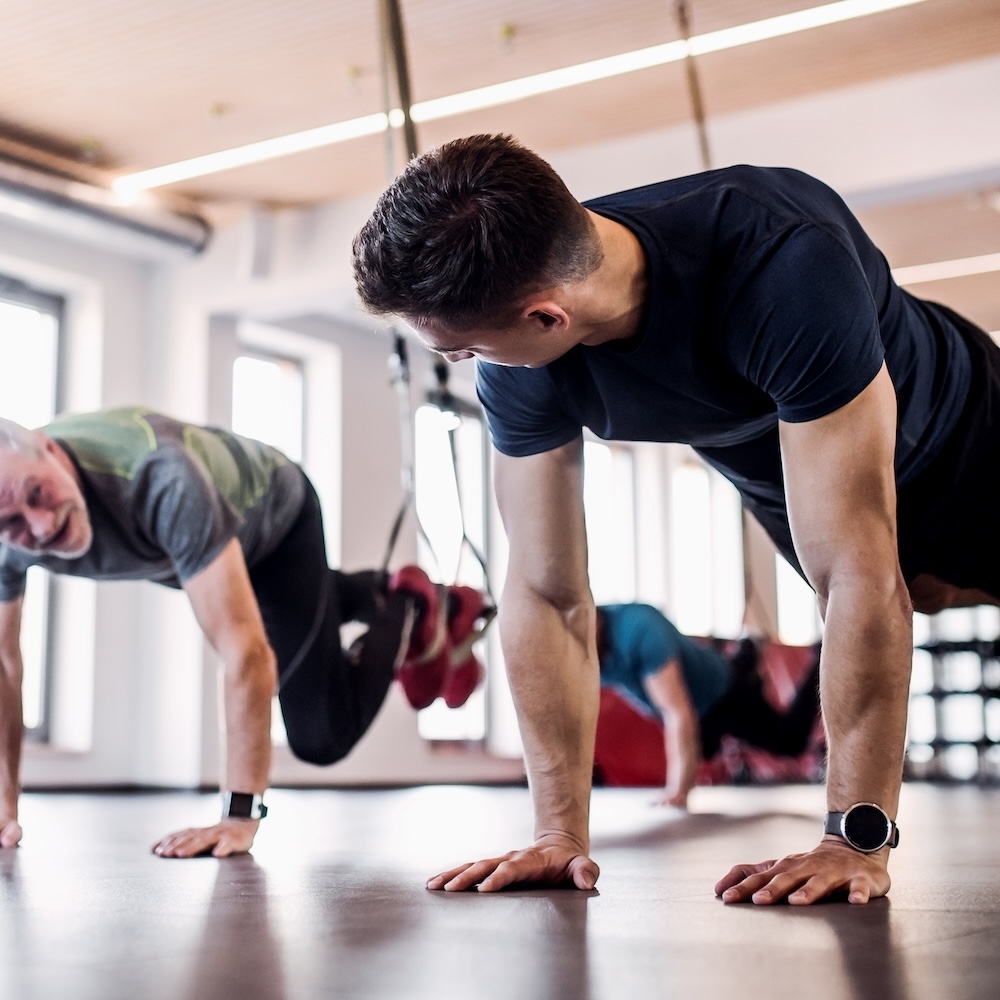 A group of cheerful seniors in gym with a young personal trainer doing exercise with TRX.