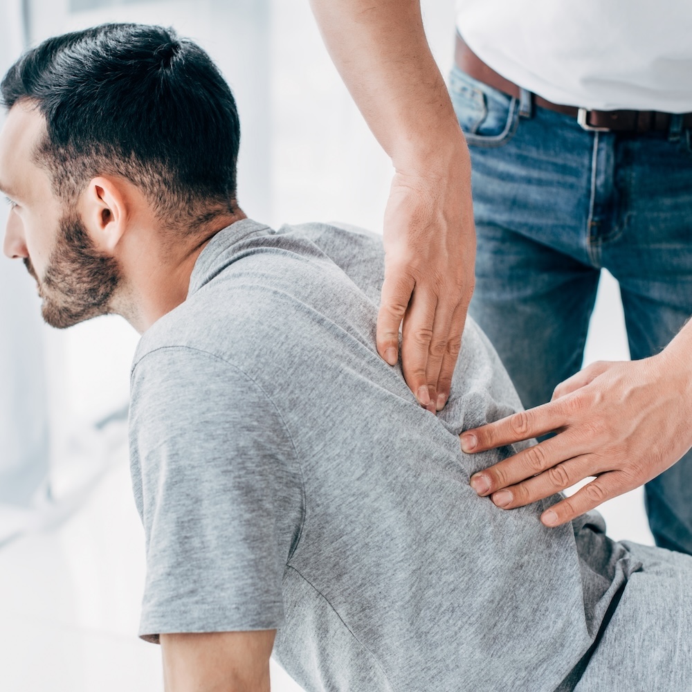 chiropractor massaging back of bearded man in hospital