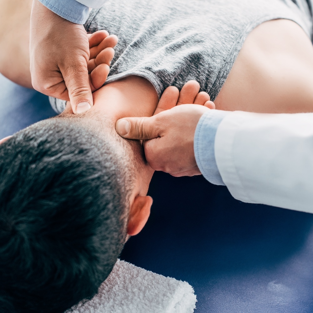 chiropractor massaging neck of man lying on Massage Table with towel